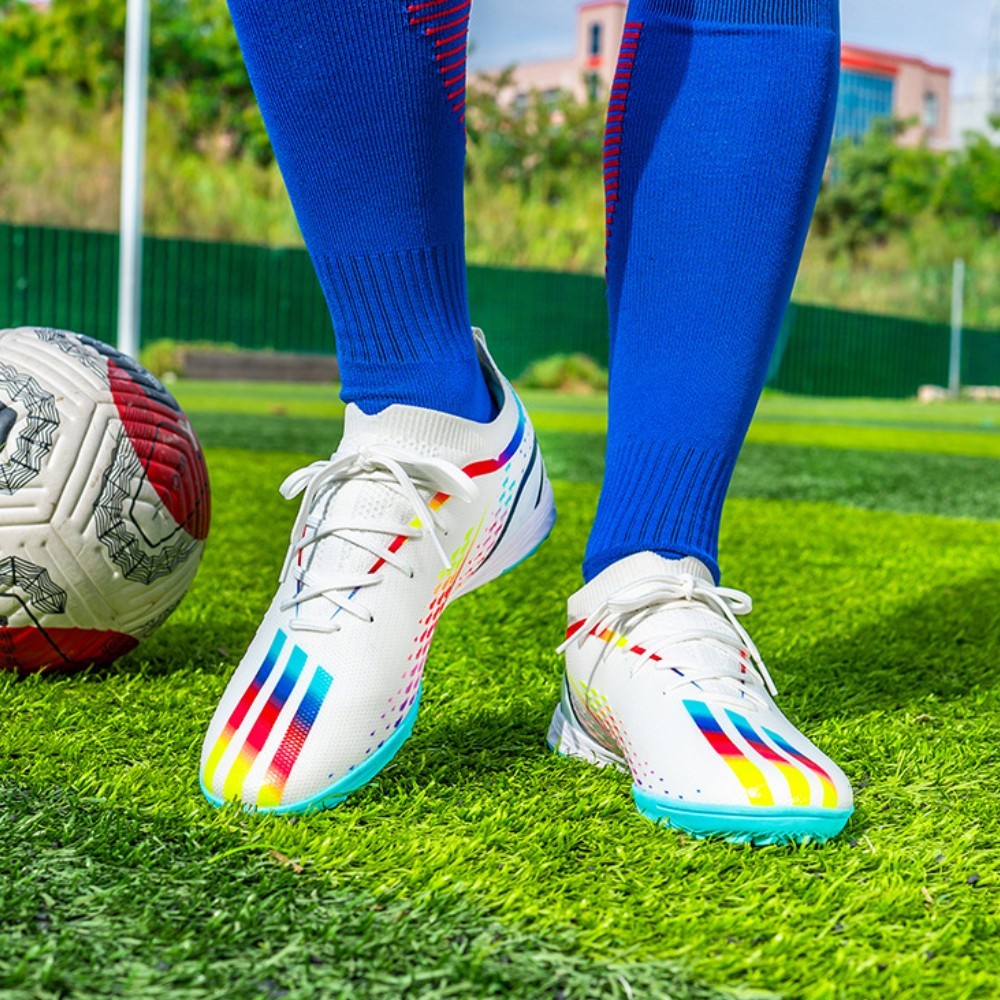 White soccer cleats with colorful stripes on grass next to a soccer ball